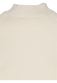 Jersey de color beige claro con cuello alto acanalado y mangas rangl�án. Textura suave con un acabado liso y sin patrones ni detalles visibles.