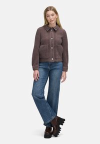 Brun tekstureret cropped jakke med knaplukning, to store lommer og spidse krave, parret med brede jeans og solide brune støvler.