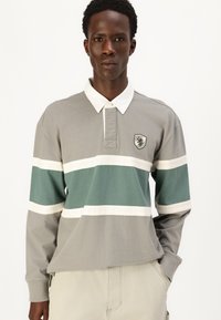 Long-sleeve polo shirt in gray with teal and white horizontal stripes, featuring a collar and a shield logo on the left chest.