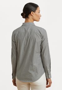 Raitapaita pitkähihaisia mustavalkoisena, jossa on nappikiinnitys kauluksessa, kaareva helma ja napitettavat hihansuut. Pehmeä puuvillakangas.