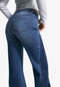 Jeans en denim bleu foncé avec une taille haute, des jambes droites et deux poches arrière. Présente des coutures discrètes et un design classique.