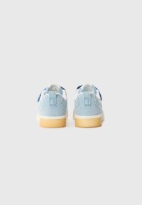 Des baskets en denim bleu clair présentent une semelle en caoutchouc blanc lisse et un dos texturé. Le design comprend des détails de couture subtils et des languettes.