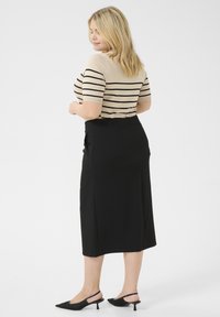 Beige gestreepte top met korte mouwen, gecombineerd met een zwarte rok tot de knie. Zwarte slingback schoenen met een spitse neus. Gladde texturen overal.