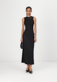 Zwarte mouwloze top met een getailleerde pasvorm en een zilveren kettingaccent, gecombineerd met een lange zwarte rok en zwarte puntige pumps.