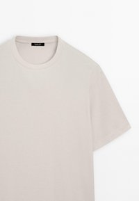 Białe beżowe krótkie rękawy, t-shirt z okrągłym dekoltem i czarną metką wewnątrz kołnierzyka, na której jest napis „Massimo Dutti”.