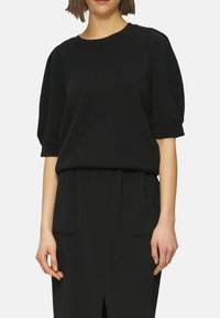 Top noir en coton mélangé avec des manches courtes et bouffantes et un col arrondi. Présente une coupe décontractée et des détails de couture subtils.