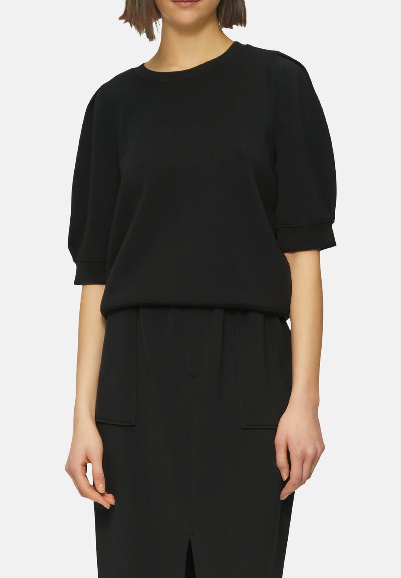 Top noir en coton mélangé avec des manches courtes et bouffantes et un col arrondi. Présente une coupe décontractée et des détails de couture subtils.