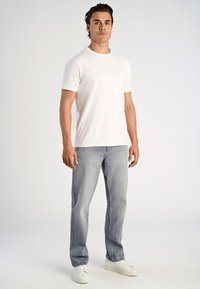 Biała koszulka z krótkim rękawem w połączeniu z jasnoniebieskimi dżinsami o prostych nogawkach oraz białymi trampkami, cechująca się prostym i czystym designem.