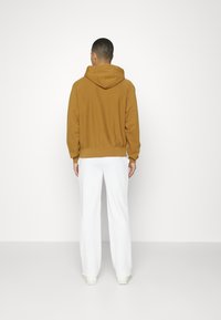 Felpa con cappuccio marrone dalla vestibilità comoda, polsini e orlo a coste, abbinata a pantaloni bianchi larghi. Texture liscia.