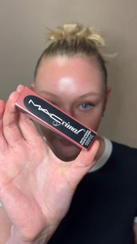 Personne aux cheveux clairs en chignon tient une boîte du produit pour les lèvres MAC Animal près de la caméra, masquant partiellement son visage.