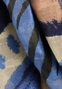 Textil s abstraktními vzory v odstínech modré, černé a náznacích broskvové. Vzorek tkaniny připomínající mřížku a vrstvená struktura látky.