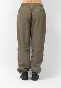Leichte, olivgrüne Cargo-Hosen mit elastischem Bund, Reißverschluss-Tasche an der Rückseite und schmal zulaufenden Beinen, kombiniert mit schwarzen Wanderschuhen.