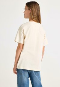 Krämfärgad bomullströja med korta ärmar och rak skärning, kombinerad med blå denimjeans som har en avslappnad passform och enkel design.