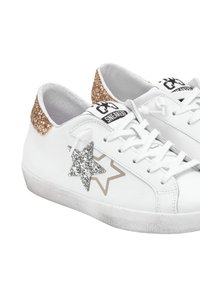 Sneakers bianchi con tacco dorato scintillante, accentuato da una stella argentata e contorno della stella grigia chiaro. Pelle testurizzata e suola in gomma.