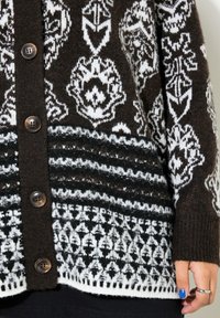 Stickad cardigan med ett mönster i brunt, vitt och svart, texturerad tyg och mörka knappar. Accenter inkluderar geometriska mönster och ränder.