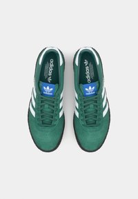 Adidași verzi din suede, cu accente albe în trei dungi, logo albastru pe limbă și talpă din cauciuc negru. Design cu șireturi, cu textură perforată.