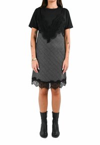 Top in pizzo nero a maniche corte, abbinato a una gonna a quadri grigia strutturata con bordo in pizzo. Indossato con stivaletti neri alla caviglia.