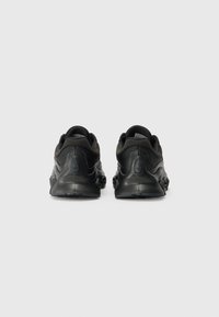 Des baskets noires avec une tige texturée, des accents lisses et une silhouette arrondie. Elles présentent un talon proéminent et une semelle en caoutchouc à motifs.