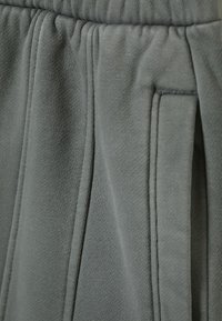 Pantaloni de trening gri dintr-un material moale. Include buzunare laterale, o suprafață texturată și detalii cusute de-a lungul cusăturilor.