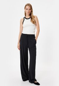 Schwarze High-Waist-Hosen mit elastischem Bund, kombiniert mit einem weißen Tanktop mit schwarzem Saum. Glatter, leichter Stoff.