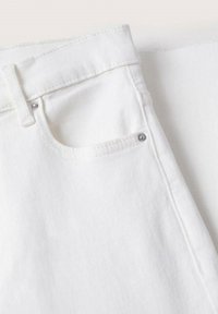 Gros plan sur un tissu en denim blanc montrant une poche avant avec des rivets en métal et une passoire pour ceinture sur la ceinture.