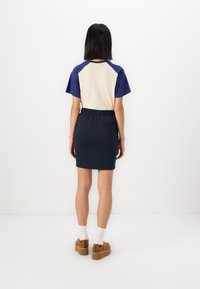 Marinblå och krämfärgad färgblock topp med korta ärmar, kombinerad med en mörk marinblå figurnära kjol med elastisk midja och två bakfickor.