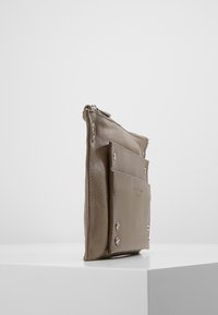 Bežová kožená taška na zip s přední kapsou a stříbrnými kovovými detaily. Kompaktní a plochý design.