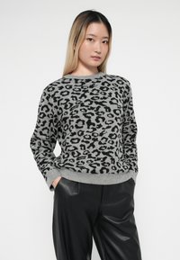 Un pull gris avec un motif léopard noir, un col et des poignets côtelés, associé à un pantalon noir à coupe ample.
