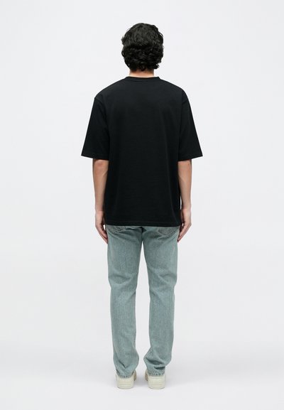 Melna īsroku T-krekls no kokvilnas, vaļējs siluets, vienkāršs dizains. Valkāts ar gaiši zilām taisnām džinsa biksēm un bēšām sporta kurpēm.