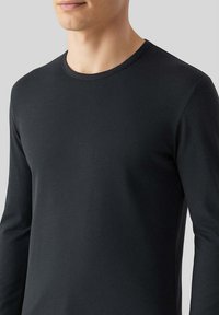 Maglietta nera a maniche lunghe realizzata in tessuto liscio con scollatura rotonda. Presenta un design aderente e dettagli di cucitura minimal.