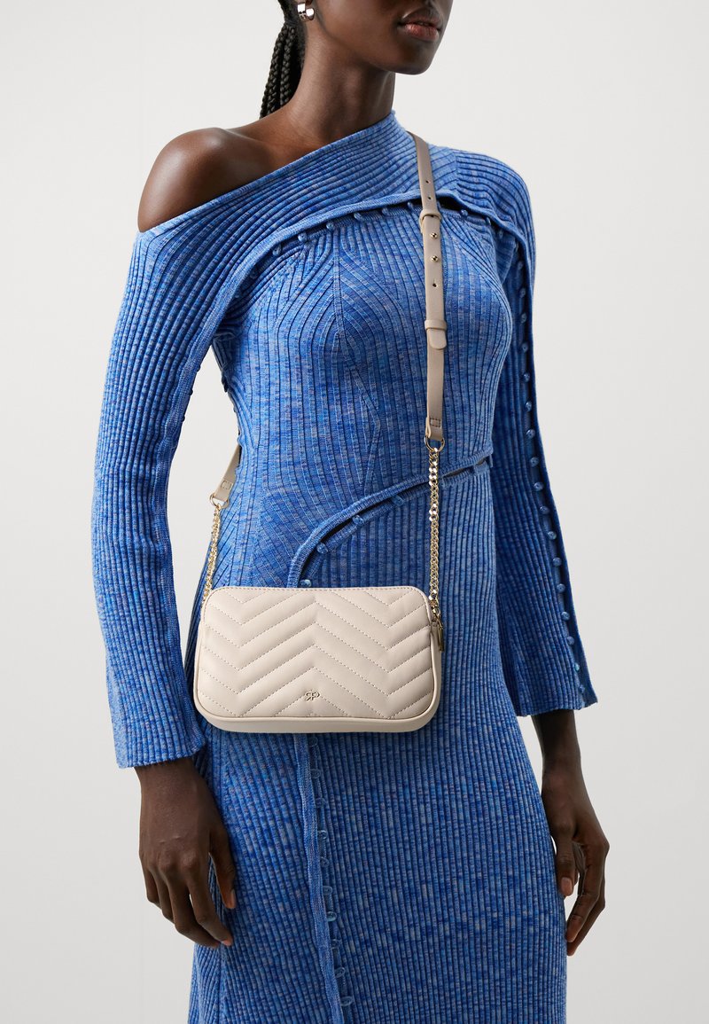 Beige quiltet.crossbody-veske med chevron-mønster, gullkjede-rem og glatt lærfinish, båret over en blå strukturert off-shoulder-kjole.