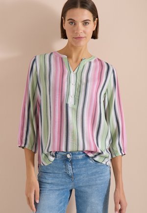 Femme portant un chemisier à rayures verticales rose, vert et noir avec des manches trois-quarts, rentré dans un jean taille haute bleu clair.