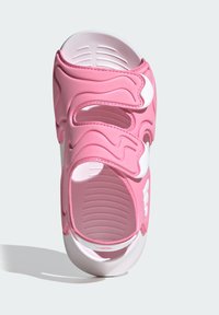 Różowa sandałka wykonana z miękkiej gumy z falistym wzorem, otwartym noskiem i trzema regulowanymi paskami. Wnętrze podeszwy z teksturą i białe akcenty.