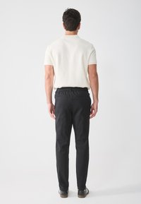White ribbed short-sleeve shirt with a classic collar paired with black elastic-waist trousers and dark leather shoes.