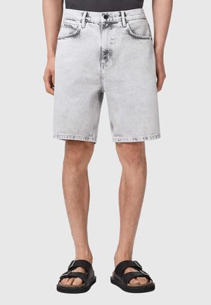 Short en denim gris clair avec poches avant, porté avec des sandales noires à boucles et un haut noir.