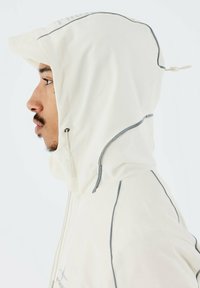 Chaqueta con capucha de color beige claro con acentos grises, que cuenta con un capó ajustable y detalles de costura lateral. Textura suave, diseño moderno.