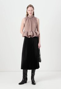 Brūns bez piedurknēm tops ar savilkta auduma un peplum apakšmalu, apvienots ar melnu plecu midi svārku un melniem zābakiem līdz ceļgaliem.