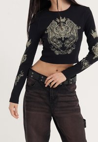 Black cropped long-sleeve shirt with intricate silver dragon and rose designs on sleeves, paired with dark denim pants and a black belt.