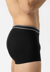 Boxers en noir avec un motif côtelé, dotés d'une ceinture élastique grise et d'une texture lisse. La vue de côté met en avant leur forme ajustée.