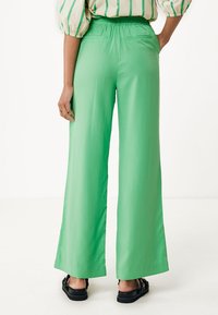 Groene wijde broek van gladde stof, met een elastische tailleband en twee achterzakken. De zoom is recht en reikt tot op de vloer.
