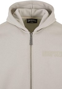 Beige zip-up hoodie with a drawstring hood, made of soft fabric. Features a branded label on the inside and discreet logo embroidery.