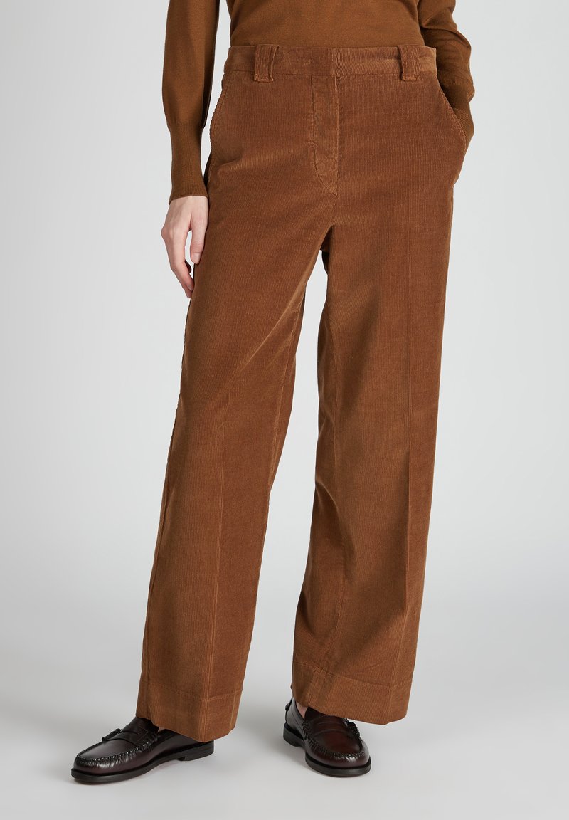 Bruine corduroy wijde broek met een gestructureerd oppervlak, voorzien van zijzakken en een hoge taille. Gecombineerd met donkerbruine instappers.