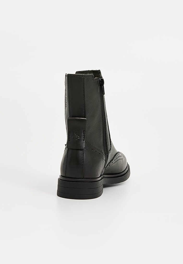 Zwarte leren enkelboot met een gestructureerde afwerking, zijritssluiting en een lage blokhak. Decoratieve brogue-details langs de neus.