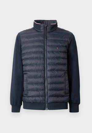 Marineblå quiltet jakke med fuld frontlynlås, høj krave, ribbede manchetter og lille flaglogo på brystet.