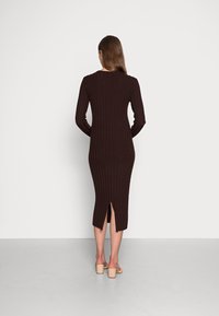 Abito lungo a maniche con righe marroni in maglia, con una silhouette aderente e uno spacco posteriore, abbinato a sandali con tacco quadrato beige.