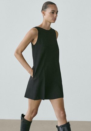 Abito nero senza maniche con silhouette dritta, tasche laterali e una texture liscia, abbinato a stivali neri al ginocchio.