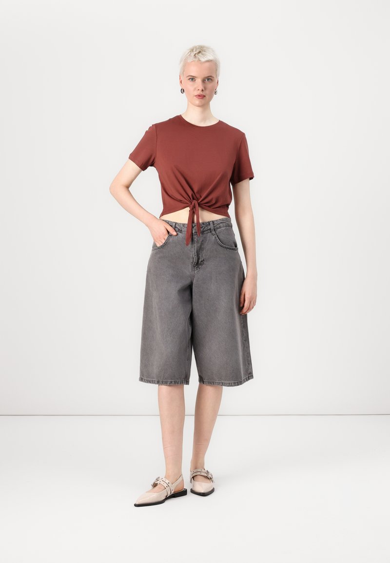 Camiseta de rayas con nudo delantero, culottes de mezclilla gris y bailarinas beige. Forma simple y ajuste relajado, con detalles y texturas mínimas.