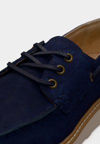 Casual παπούτσι από μπλε σουέντ με σκούρα κορδόνια περασμένα από ορείχαλκα ριγέ και ταμπά σόλα με λευκά ραφές.