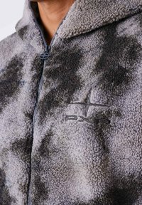 Fleece zip-up jack in grijs en zwart met een zachte, gestructureerde oppervlakte. Heeft een geborduurd logo en een gevoerde capuchon voor extra warmte.
