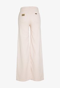 Růžové široké nohavice z měkké látky, které mají dvě zadní kapsy s malými obdélníkovými hnědými štítky pro identifikaci značky.